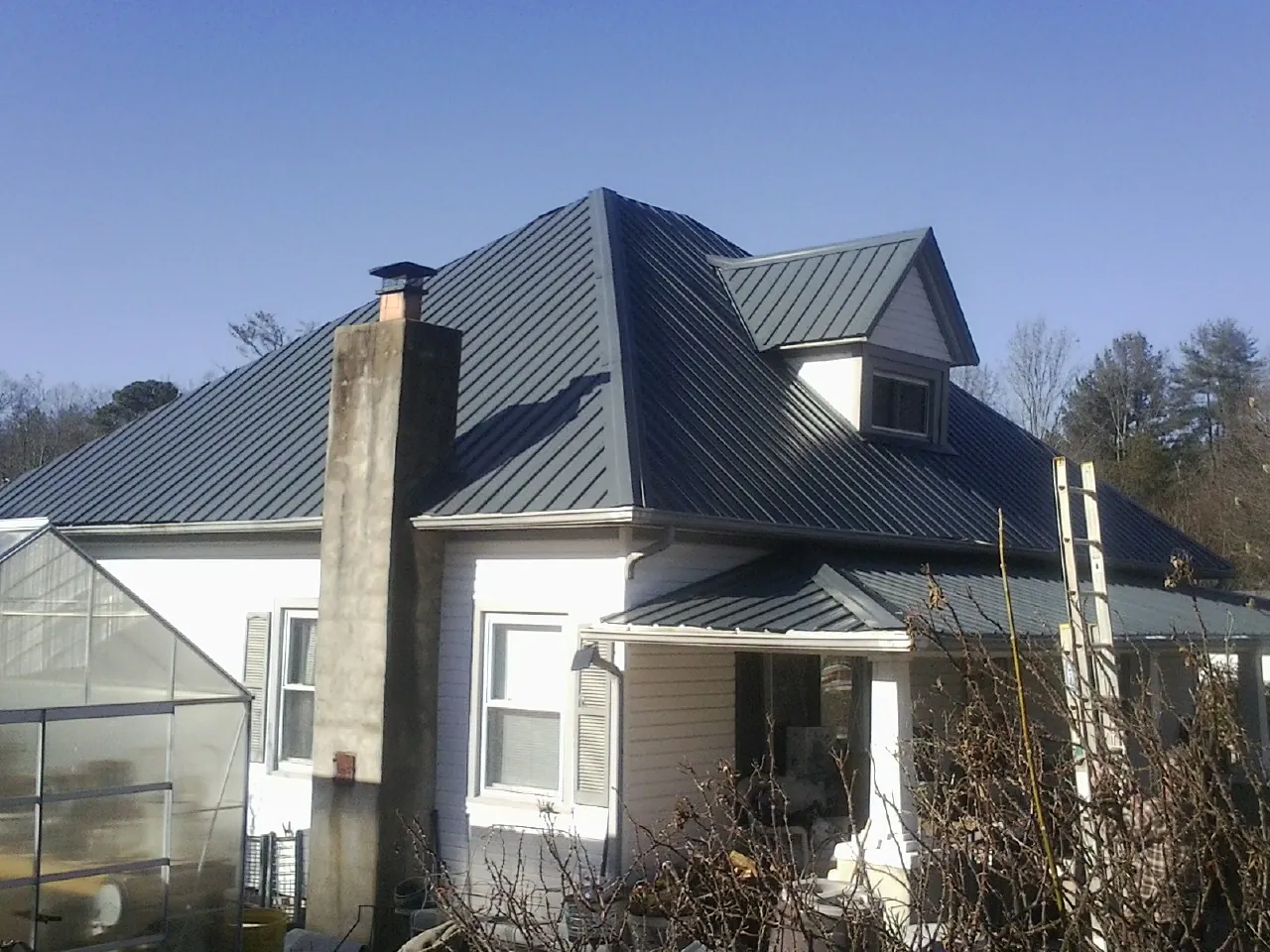 Dark blue standing seam metal roof on a white farmhouse with dormer — Slate & Tile Roof Repair by Roofing Brothers in Ellenboro