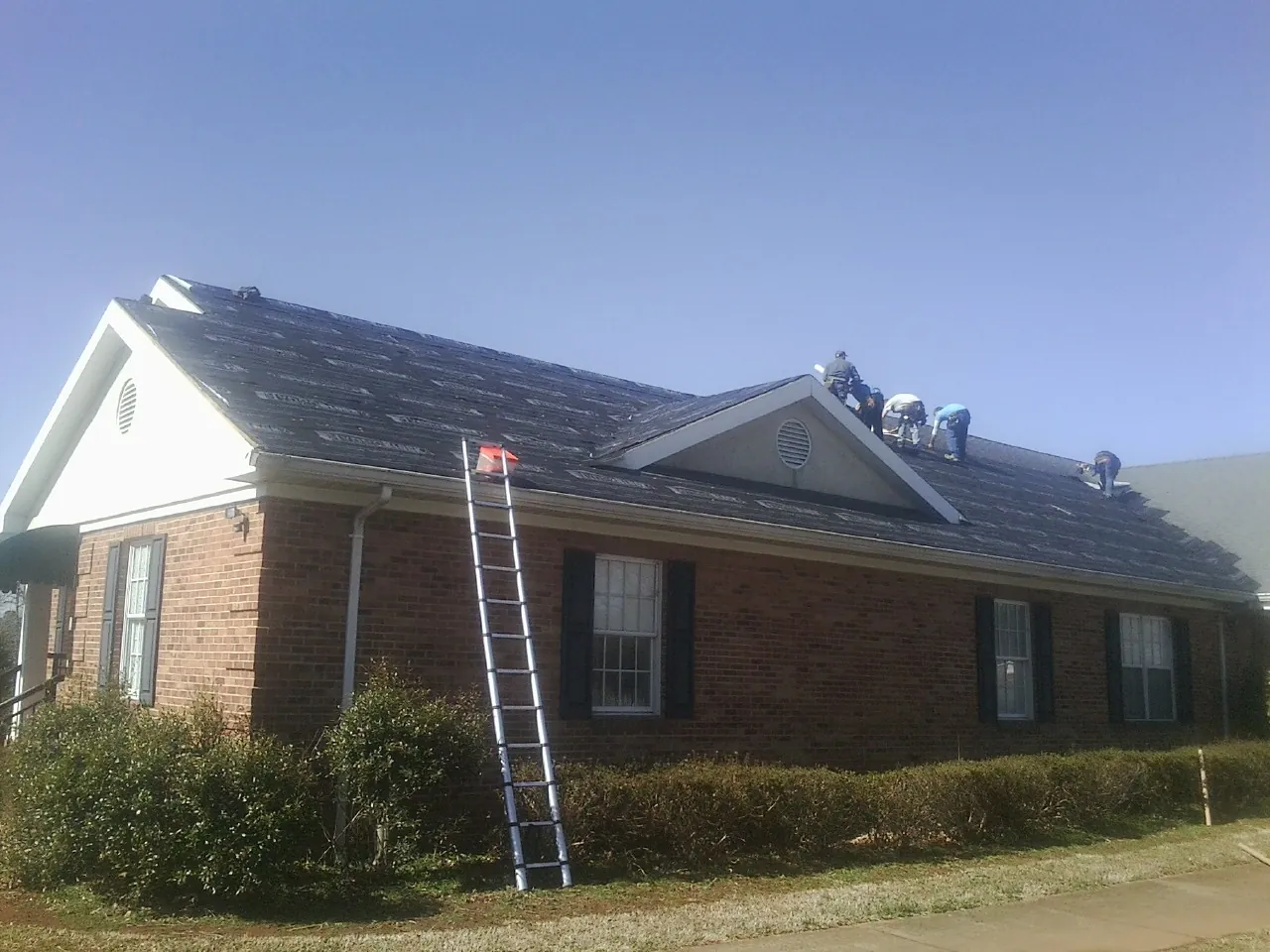 Crew tearing shingles off a brick ranch roof with a ladder set — Metal Roof Repair work by our crew in Ellenboro