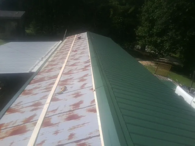 Old rusted panels beside newly installed green metal roofing — Wind Damage Roof Repair by Roofing Brothers in Ellenboro