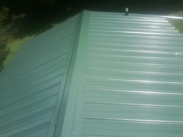 New green metal panels meeting at the ridge of a roof — Flat Roof Repair work by our crew in Ellenboro