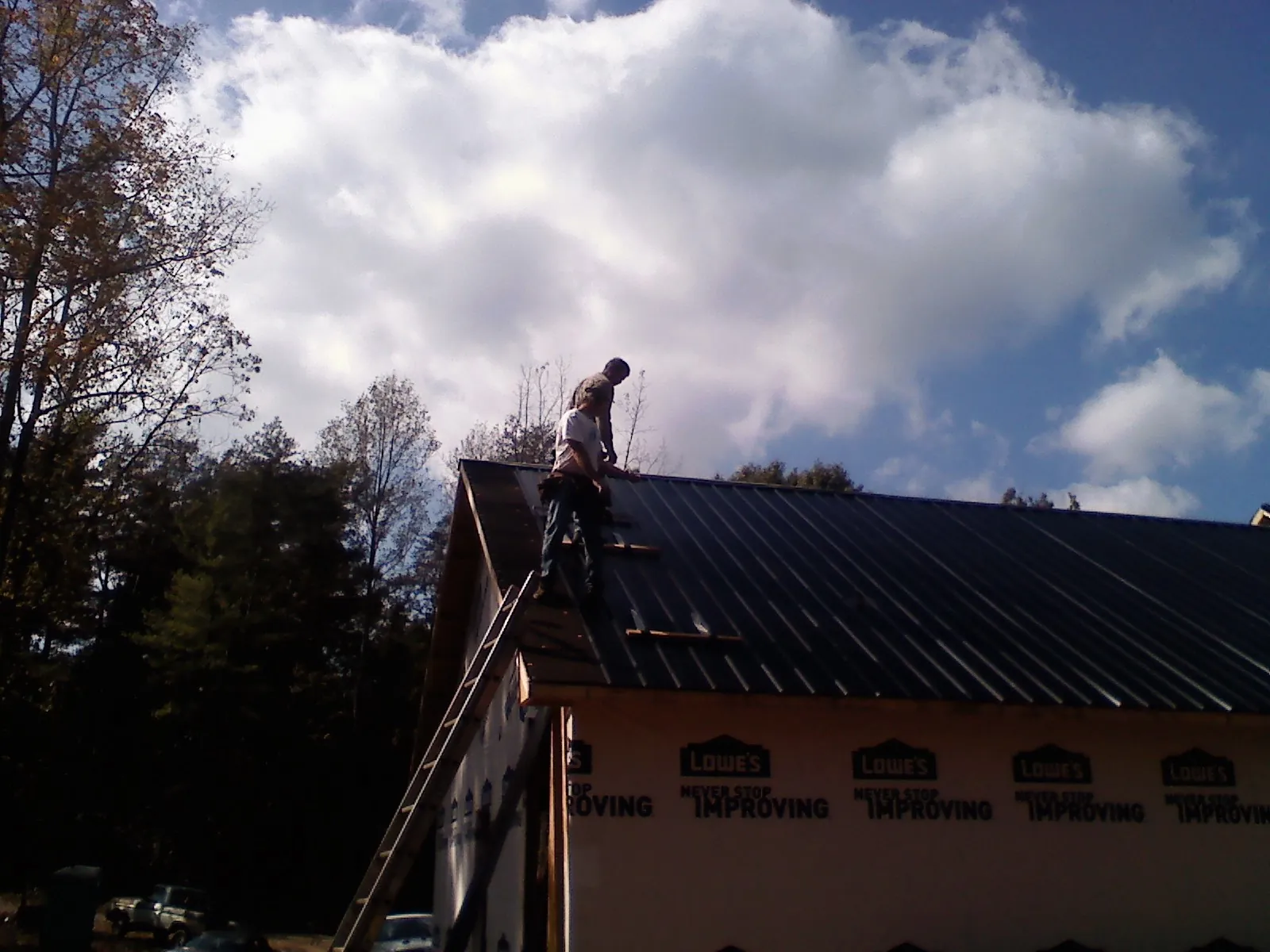 Roofer fastening dark metal panels high against a cloudy sky, from a Roof Inspection job in Ellenboro