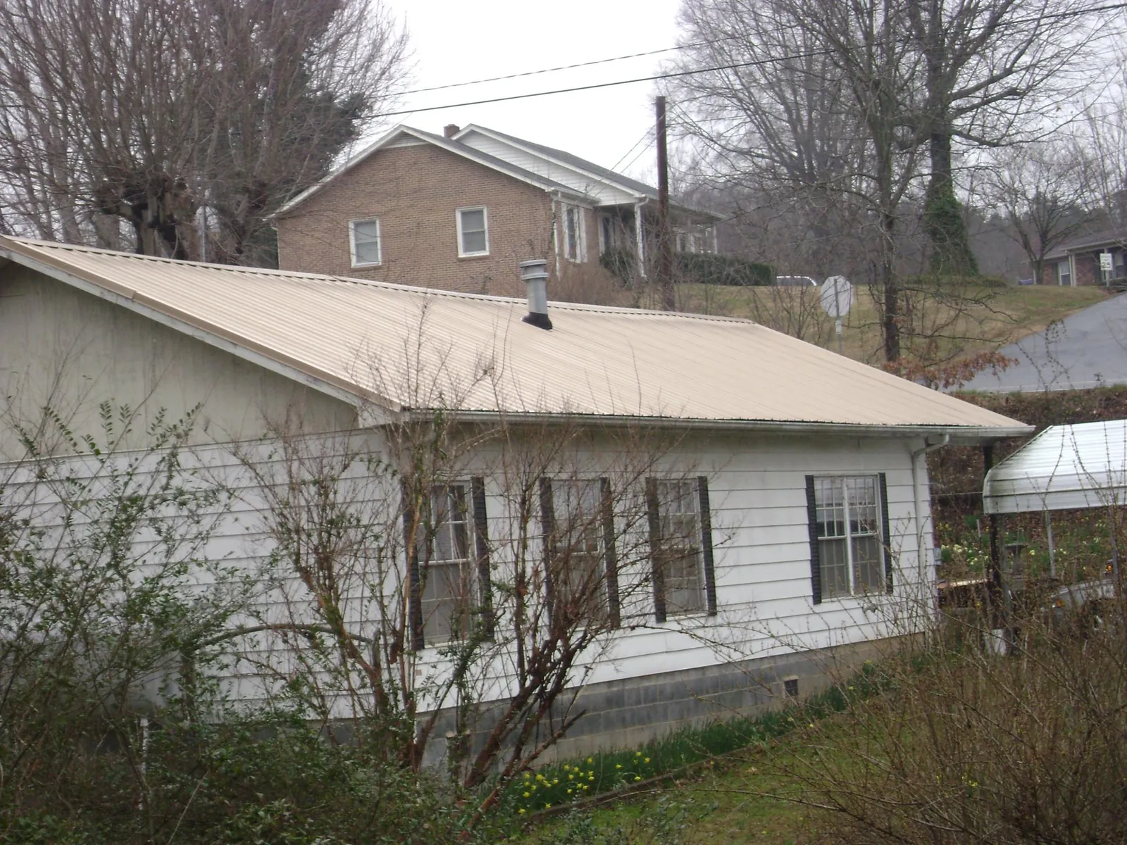 Tan metal roof on a white sided house set into a hillside — Commercial Roofing by Roofing Brothers in Ellenboro